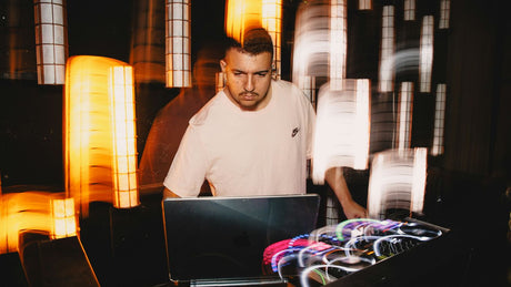 Dj performing with laptop and equipment at night.