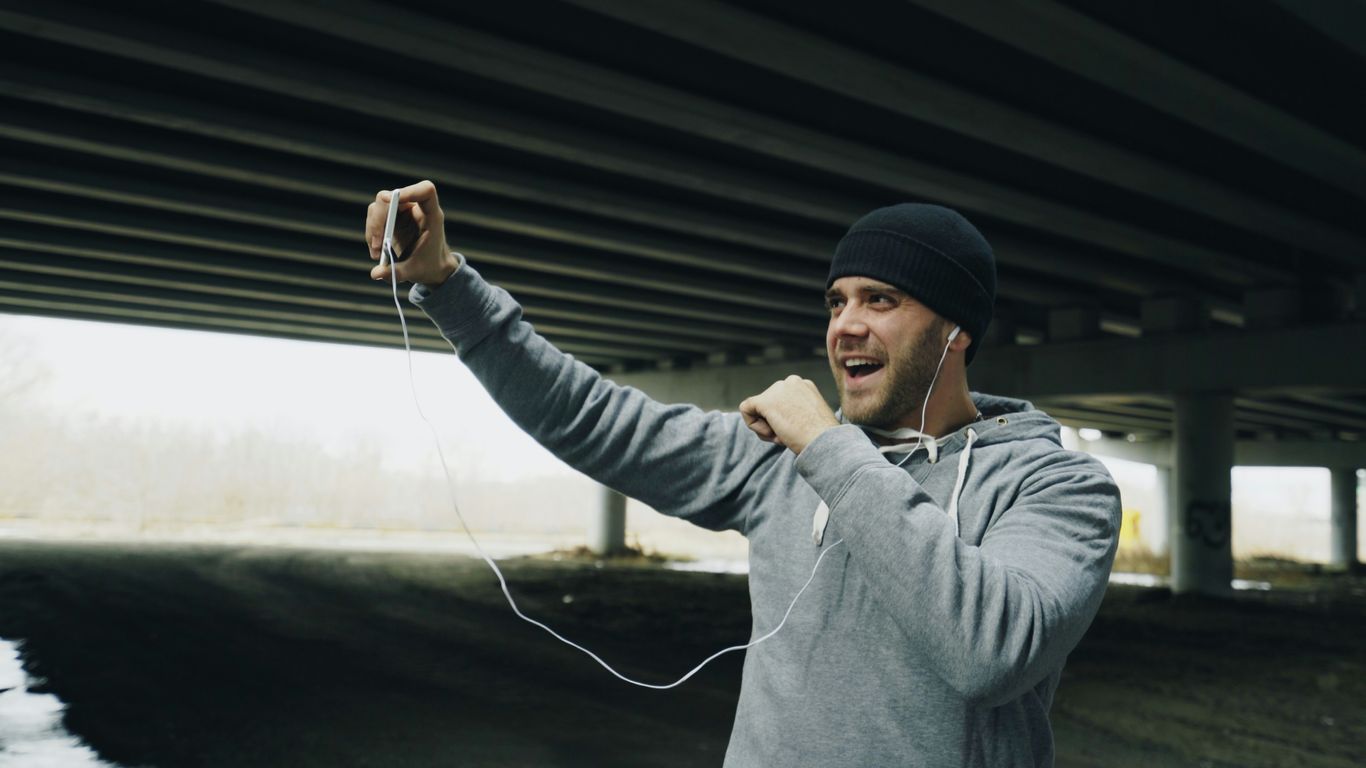 Man in beanie and hoodie singing into phone