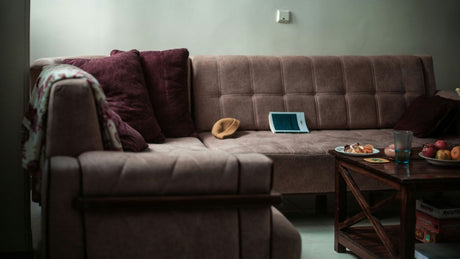 A sectional sofa with pillows and a tablet on it.
